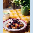 Ein Teller mit French Toast, Beeren und Sahne, dazu eine Tasse Tee und eine Vase mit Blumen auf kariertem Tuch.