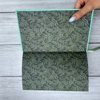 Kein Text sichtbar. Eine geöffnete Notizbuchseite mit grünem Farnmuster. Eine Hand hält die Seite.