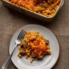 Kein Text im Bild. Es zeigt einen Teller mit Käsesauce-Nudeln und Fleisch, daneben eine geschichtete Auflaufform.