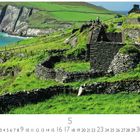 „Slea Head“ und Monatszahlen. Ruinen aus Stein umgeben von grünen Hügeln mit Meerblick.