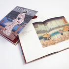 „Sommergewitter“ von Yosa Buson, daneben ein aufgeschlagenes Buch mit japanischer Illustration von Personen mit Regenschirmen.