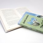 "The Call of the Wild" von Jack London. Ein geschlossenes Buch liegt auf einem offenen Buch, welches auf Seite 62 ist.