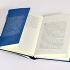 Offenes Buch mit Text auf den Seiten 82 und 83, linker blauer Einband enthält zusätzlichen Text.