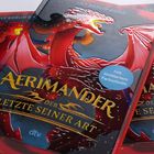 "Buchtitel: 'AERIMANDER. Der Letzte Seiner Art'. Roter Drache auf dem Cover, gelbe Schrift, blaues Etikett: 'Mit limitiertem Farbschnitt'."