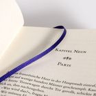 Kapitel Neun: Paris. Offenes Buch mit blauem Leseband auf der Seite.