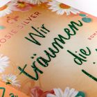 „Wir träumen die Liebe“, Autor Josie Silver, umgeben von Blumen auf einem orangefarbenen Hintergrund.