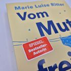 Text: "SPIEGEL Bestseller-Autorin". Cover eines Buches, helle Farbe, blauer Text, Wäscheleine mit blauer Unterwäsche.