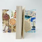 Zwischen zwei illustrierten Karten steht ein aufgeschlagenes Buch. Links sind Kuchen, rechts ein Leuchtturm zu sehen.
