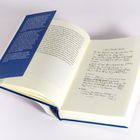 Eine aufgeschlagene Buchseite. Links blauer Einband mit Text, rechts handgeschriebene Notizen.