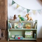 Ein Regal mit Kinderbüchern wie "Kleine Schildkröte" und "Kleiner Löwe". Oben Kuscheltiere, bunte Wimpel darüber.