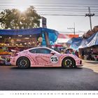 "73" auf pinkem Auto mit Aufschriften wie "SCHNITZEL" und "KOTLETT", steht auf Marktstraße mit bunten Ständen.