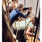 "05" steht links unten über einer Monatsübersicht. Drei Personen arbeiten an Bord eines Segelschiffs, umgeben von Seilen.