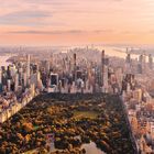 Eine Stadtansicht bei Sonnenuntergang mit einem großen zentralen Park, umgeben von Wolkenkratzern und Flüssen.