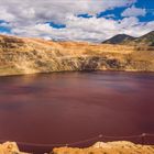 „Aber für ein paar Jahre haben wir einen prächtigen Gewinn erwirtschaftet, das sollte man nicht vergessen.“ Eine riesige Grube mit rotem Wasser, umgeben von gestuften Erdwänden und bewölktem Himmel.