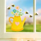 Gelbe Gießkanne mit Herz und Blumen, umgeben von Bienen. Darunter brennen drei bunte Kerzen.