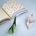 Ein Buch mit floralen Mustern, daneben zwei Origami-Kraniche aus buntem Papier, einer grün, der andere blumig.