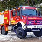 Text: "FEUERWEHR FISCHBACHAU" und "FEUERWEHR" auf einem leuchtend roten Feuerwehrfahrzeug im Schnee.