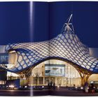 Das Bild zeigt ein modernes Gebäude mit einer wellenförmigen, leuchtenden Dachstruktur bei Nacht.