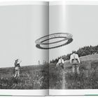 Eine fliegende scheibenförmige Struktur über einer Wiese, beobachtet von vier Männern in altmodischer Kleidung.