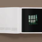 Eine Buchseite mit Textabsätzen unten links und einem Foto rechts zeigt ein Gitterfenster mit grünem Licht.