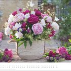 „MAI“ in Großbuchstaben unten rechts, großer Blumenstrauß in einem rustikalen Korb, verschiedene Rosen und Blüten.