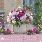 „Mai“ steht oben links, darunter ein Kalender. Üppiges Blumenarrangement in einem Korb im Freien.