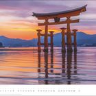 MAI. Ein traditionelles japanisches Torii-Tor steht im Wasser vor einem farbenfrohen Sonnenuntergang mit Bergen im Hintergrund.