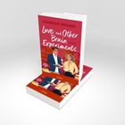 Text "LOVE AND OTHER BRAIN EXPERIMENTS" auf rosa Hintergrund, zwei Personen illustriert in einer Bibliothek, darunter "Lübbe".