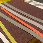 Mehrere farbige Papierstreifen auf einem braunen Stoffbezug, angeordnet in diagonalen Reihen.