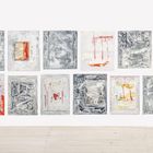 Zwölf abstrakte Gemälde in zwei Reihen an einer weißen Wand, mit roten und grauen Farbmustern.