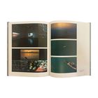 Eine offene Buchseite mit mehreren Fotografien von Landschaften, Booten und Projektionen in einer Galerie.