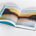 Text: "frühmorgens". Illustration eines Sees im Morgenlicht mit Bäumen im Hintergrund und einem spritzenden Fisch.