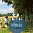 IN DER NATUR. Menschen spazieren mit einem Alpaka durch einen Waldweg, umgeben von Bäumen und Wiesen.