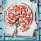 Kalenderseite mit Ziffern 5 bis 31. Erdbeerkuchen mit Sahne auf Papier und zwei Löffeln auf rustikalem, blauen Holz.