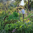Der Schriftzug „Garten“ steht inmitten blühender Pflanzen und Wiesen. Eine Gießkanne hängt dekorativ an einem Ast.