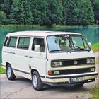 Kennzeichen: WS BJ 90. Weißer VW-Bus steht auf einer Straße, im Hintergrund ein See und Bäume.