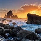 Sonnenuntergang über einer Felsenküste, mit starken Wellen und einem dramatischen, orangefarbenen Himmel.