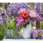 05, 01 SAM, 02 SON, 03 MON; Vase mit rosa, gelben Blumen, Flieder, Topf mit Traubenhyazinthen vor Holzzaun.