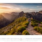 05, Naturpfad auf einem grünen Bergkamm bei Sonnenuntergang, umgeben von beeindruckenden, zerklüfteten Bergen.