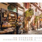 Tafeltext: "Wine and Food, Tagliere per Due €2,90." Kleine Straße mit Delikatessengeschäft, Außenbestuhlung und Pflanzen.