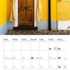 2027, Mai, Wochentage auf Deutsch und Englisch. Gelbe Wand, braune Tür, gestreifte Vorhänge, schwarzes Rohr.