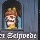 "Schwedischer Drill" erklärt Ursprung von "Alter Schwede". In Wismar Wirtshausname. Statue mit Helm schaut aus Fenster.