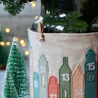 Nummern 10 bis 15 auf Filz-Stadtmotiven, grüne Tannenzweige in Glasvase, kleine künstliche Tannenbäume.