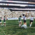 Spielszene mit Frauen in Fußballtrikots; Zuschauertribünen im Hintergrund mit mehreren Werbebannern.