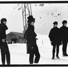 „Vier Klassen–Betriebsgelände“ auf Holzschild. Vier junge Männer in dunkler Kleidung stehen im Schnee.