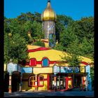 ROMANUS HAUS ESSEN. Buntes Gebäude mit goldener Kuppel, kreativ gestaltet, umgeben von Bäumen. Darunter die Zahlen 1–31.