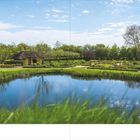 Seitenzahlen 60 und 61. Ein Teich reflektiert den Himmel in einer großen, grünen Gartenlandschaft mit Pfaden und blühenden Büschen.