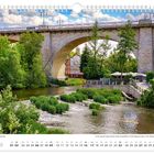 “Mai”. Hauptpier unter der Friedensbrücke. Ein Fluss fließt unter einer steinernen Brücke, umgeben von üppigem Grün.