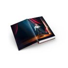 Offenes Buch mit Illustration: Eine Figur steht auf einer Bühne mit rotem Vorhang und Säule, beleuchtet von Lichtstrahlen.