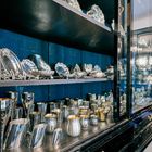 Ein Schrank mit Glasfront zeigt glänzende silberne Becher, Krüge und Schalen auf dunklen Regalböden.